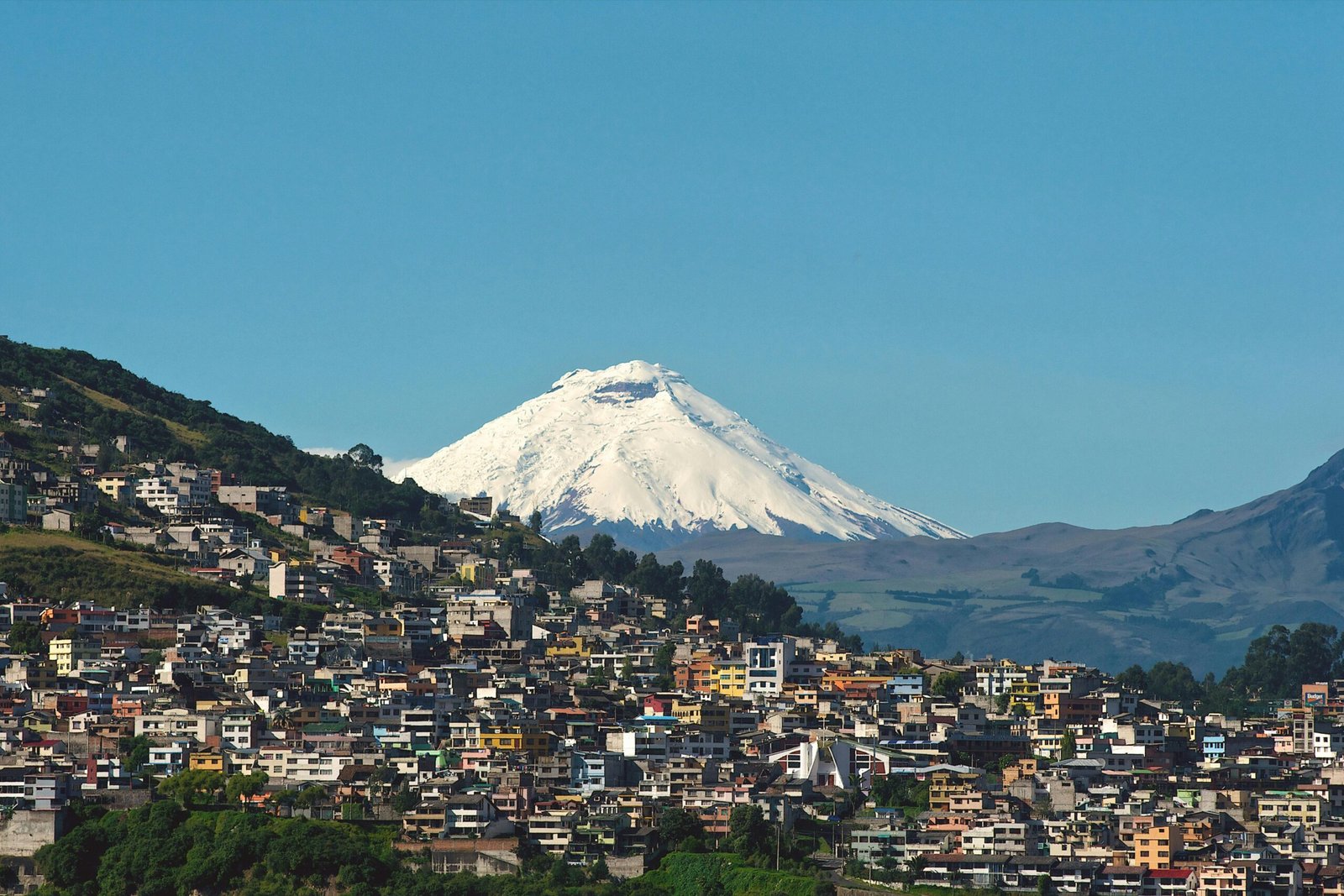 Explore Quito with the majestic backdrop of Cotopaxi Volcano under a clear blue sky.